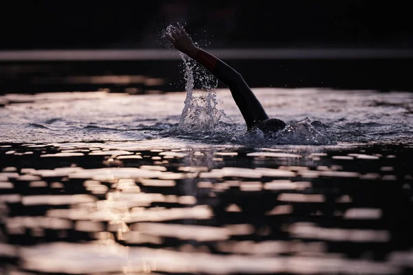 Atleta de triatlón nadando en el lago al amanecer usando traje de neopreno — Foto de Stock