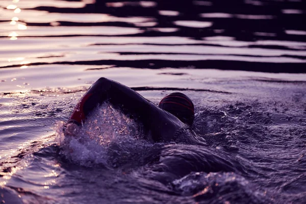 Triathlon athlete swimming on lake in sunrise wearing wetsuit — Stock Photo, Image