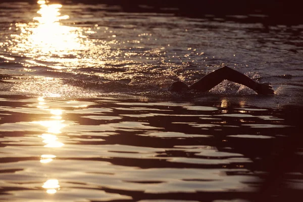 Triatlon atléta úszás tavon napkeltekor búvárruhában — Stock Fotó