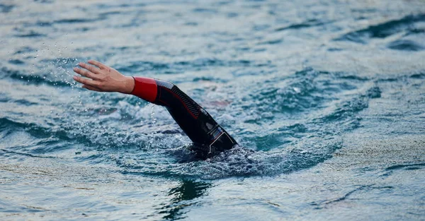 Atleta di triathlon che nuota sul lago all'alba indossando la muta — Foto Stock
