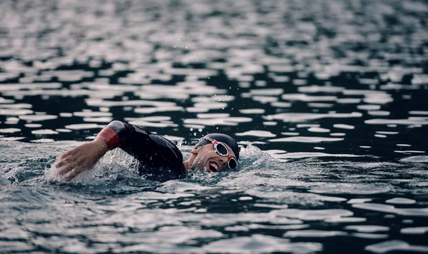 Triathlet schwimmt bei Sonnenaufgang im Neoprenanzug auf See — Stockfoto