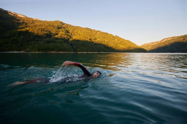 Atleta de triatlón nadando en el lago al amanecer usando traje de neopreno —  Fotos de Stock