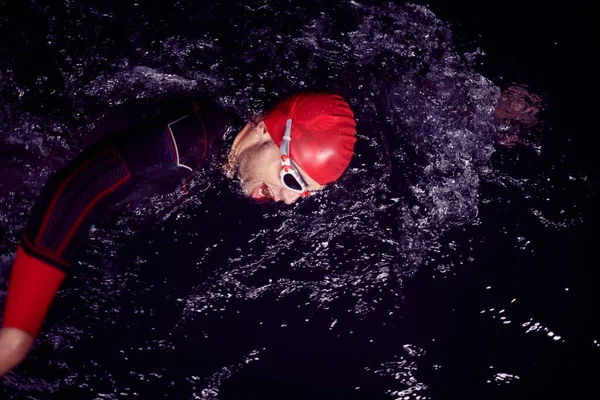 triathlon athlete swimming in dark night wearing wetsuit