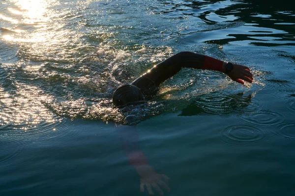 Triatlon atléta úszás tavon napkeltekor búvárruhában — Stock Fotó