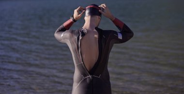 Reak triatlon atleti hazırlanıyor ve gölde yüzme eğitimi için gözlük, şapka ve dalış kıyafeti hazırlıyor.