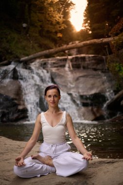 Nilüfer çiçeğinin altında oturan genç kadın sakin bir güçle meditasyon yapıyor ve doğal enerji sükuneti ve iç denge ile tamamen bağlantılı.