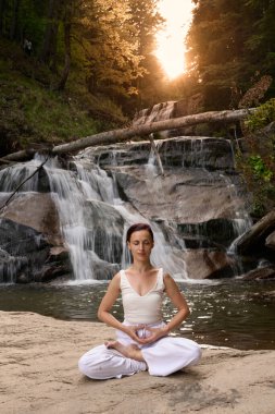 Nilüfer çiçeğinin altında oturan genç kadın sakin bir güçle meditasyon yapıyor ve doğal enerji sükuneti ve iç denge ile tamamen bağlantılı.