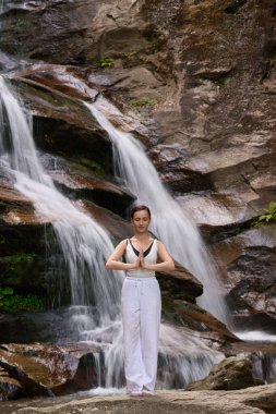 Güzel genç bir kadın gün batımında şelale ve nehir kenarında ağır ağır tai chi hareketleri yapıyor. Doğadaki uyum dengesini ve uygunluğu yakalıyor.