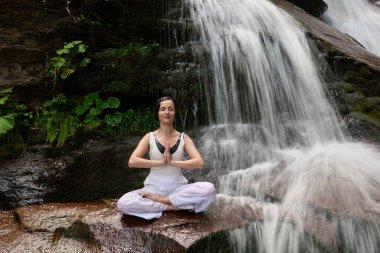 Nilüfer çiçeğinin altında oturan genç kadın sakin bir güçle meditasyon yapıyor ve doğal enerji sükuneti ve iç denge ile tamamen bağlantılı.
