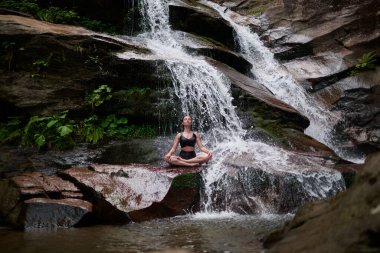 Nilüfer çiçeğinin altında oturan genç kadın sakin bir güçle meditasyon yapıyor ve doğal enerji sükuneti ve iç denge ile tamamen bağlantılı.