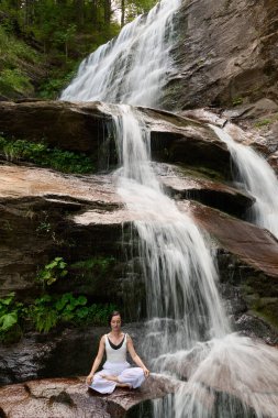 Nilüfer çiçeğinin altında oturan genç kadın sakin bir güçle meditasyon yapıyor ve doğal enerji sükuneti ve iç denge ile tamamen bağlantılı.