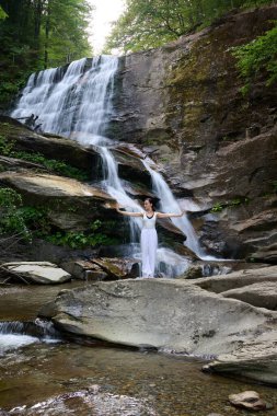 Güzel genç bir kadın gün batımında şelale ve nehir kenarında ağır ağır tai chi hareketleri yapıyor. Doğadaki uyum dengesini ve uygunluğu yakalıyor.