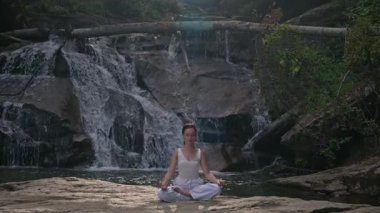 Nilüfer çiçeğinin altında oturan genç kadın, sakin bir güçle meditasyon yapıyor ve doğal enerji sükuneti ve iç denge ile tamamen bağlantılı. Yavaş çekim sinematik çekim