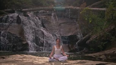 Nilüfer çiçeğinin altında oturan genç kadın, sakin bir güçle meditasyon yapıyor ve doğal enerji sükuneti ve iç denge ile tamamen bağlantılı. Yavaş çekim sinematik çekim