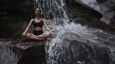 Nilüfer çiçeğinin altında oturan genç kadın, sakin bir güçle meditasyon yapıyor ve doğal enerji sükuneti ve iç denge ile tamamen bağlantılı. Yavaş çekim sinematik çekim