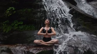 Nilüfer çiçeğinin altında oturan genç kadın, sakin bir güçle meditasyon yapıyor ve doğal enerji sükuneti ve iç denge ile tamamen bağlantılı. Yavaş çekim sinematik çekim