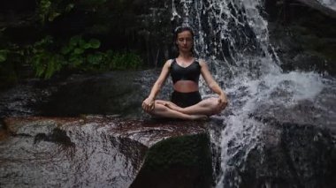 Nilüfer çiçeğinin altında oturan genç kadın, sakin bir güçle meditasyon yapıyor ve doğal enerji sükuneti ve iç denge ile tamamen bağlantılı. Yavaş çekim sinematik çekim