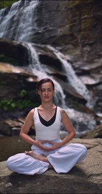 Lotus 'ta oturan kadın, tropikal şelale altında poz veriyor sakin bir güç ve farkındalık ile doğa enerjisi sükuneti ve iç dengesi ile bütünüyle bağlantılı. Ağır çekimin dikey videosu