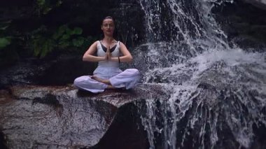 Nilüfer çiçeğinin altında oturan genç kadın, sakin bir güçle meditasyon yapıyor ve doğal enerji sükuneti ve iç denge ile tamamen bağlantılı. Yavaş çekim sinematik çekim