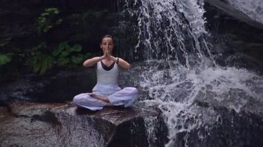 Nilüfer çiçeğinin altında oturan genç kadın, sakin bir güçle meditasyon yapıyor ve doğal enerji sükuneti ve iç denge ile tamamen bağlantılı. Yavaş çekim sinematik çekim