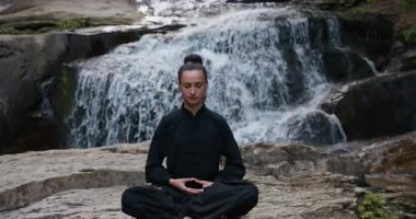 Bir kadın lotus pozisyonunda oturur, tropik bir şelalenin altında yoga ve tai chi pratik yapar, sakin bir güç ve farkındalıkla meditasyon yapar, doğanın enerjisine, sükunetine ve iç güzelliğine tamamen bağlıdır.