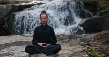 Bir kadın lotus pozisyonunda oturur, tropik bir şelalenin altında yoga ve tai chi pratik yapar, sakin bir güç ve farkındalıkla meditasyon yapar, doğanın enerjisine, sükunetine ve iç güzelliğine tamamen bağlıdır.