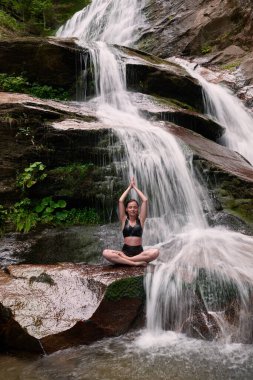 Nilüfer çiçeğinin altında oturan genç kadın sakin bir güçle meditasyon yapıyor ve doğal enerji sükuneti ve iç denge ile tamamen bağlantılı.