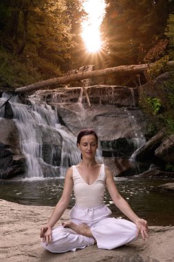 Nilüfer çiçeğinin altında oturan genç kadın sakin bir güçle meditasyon yapıyor ve doğal enerji sükuneti ve iç denge ile tamamen bağlantılı.