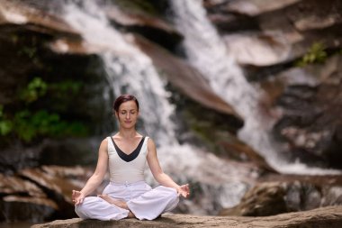 Nilüfer çiçeğinin altında oturan genç kadın sakin bir güçle meditasyon yapıyor ve doğal enerji sükuneti ve iç denge ile tamamen bağlantılı.