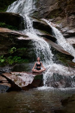 Nilüfer çiçeğinin altında oturan genç kadın sakin bir güçle meditasyon yapıyor ve doğal enerji sükuneti ve iç denge ile tamamen bağlantılı.