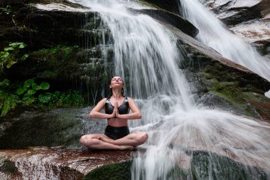 Nilüfer çiçeğinin altında oturan genç kadın sakin bir güçle meditasyon yapıyor ve doğal enerji sükuneti ve iç denge ile tamamen bağlantılı.