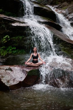 Nilüfer çiçeğinin altında oturan genç kadın sakin bir güçle meditasyon yapıyor ve doğal enerji sükuneti ve iç denge ile tamamen bağlantılı.