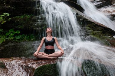 Nilüfer çiçeğinin altında oturan genç kadın sakin bir güçle meditasyon yapıyor ve doğal enerji sükuneti ve iç denge ile tamamen bağlantılı.