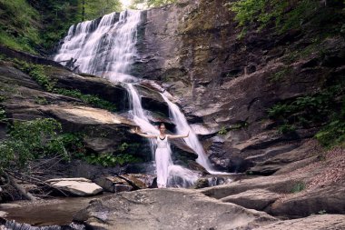 Güzel genç bir kadın gün batımında şelale ve nehir kenarında ağır ağır tai chi hareketleri yapıyor. Doğadaki uyum dengesini ve uygunluğu yakalıyor.