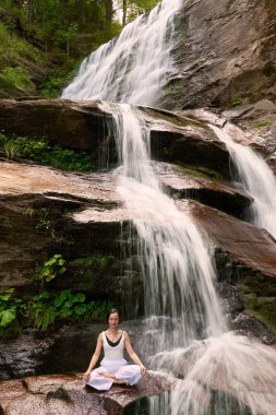 Nilüfer çiçeğinin altında oturan genç kadın sakin bir güçle meditasyon yapıyor ve doğal enerji sükuneti ve iç denge ile tamamen bağlantılı.