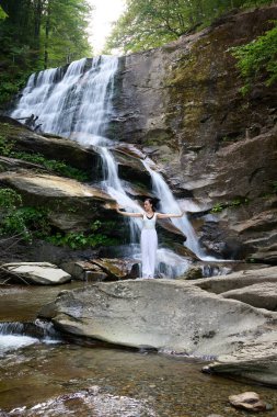 Güzel genç bir kadın gün batımında şelale ve nehir kenarında ağır ağır tai chi hareketleri yapıyor. Doğadaki uyum dengesini ve uygunluğu yakalıyor.