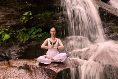 Nilüfer çiçeğinin altında oturan genç kadın sakin bir güçle meditasyon yapıyor ve doğal enerji sükuneti ve iç denge ile tamamen bağlantılı.