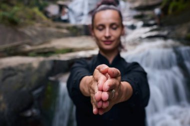 Doğada Tai Chi uygulayan, geleneksel bir siyah dövüş sanatları üniforması giyen, bir şelalenin yanında zarif bir şekilde duran, meditasyon ve dengeye odaklanmış bir kadın. Asya kültüründe sağlıklı yaşam tarzı 