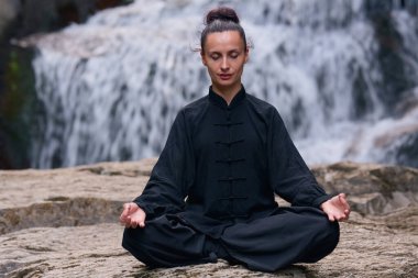 Bir kadın lotus pozisyonunda oturur, tropik bir şelalenin altında yoga ve tai chi pratik yapar, sakin bir güç ve farkındalıkla meditasyon yapar, doğanın enerjisine, sükunetine ve iç güzelliğine tamamen bağlıdır.