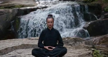 Bir kadın lotus pozisyonunda oturur, tropik bir şelalenin altında yoga ve tai chi pratik yapar, sakin bir güç ve farkındalıkla meditasyon yapar, doğanın enerjisine, sükunetine ve iç güzelliğine tamamen bağlıdır.