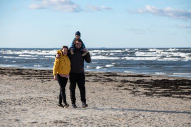 Mutlu bir aile, serin bir sonbahar plajı boyunca yürür. Genç oğulları sevinçle koşar, taze rüzgar ve dindirici dalgalar onları bir anda kucaklarken kalıcı anılar yaratır.