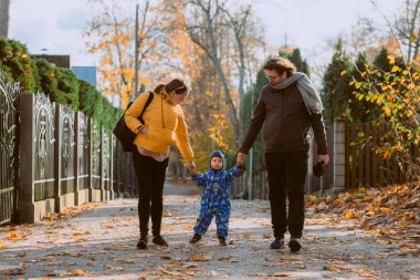 Sevgi dolu bir çift, sonbaharın canlı renkleriyle çevrili oğluyla birlikte güneşli bir parkta gezer. Neşeli ve huzurlu bir aile anının tadını çıkarırlar.