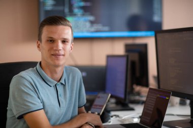 Genç bir programcı ofisinde masasında oturmuş, akıllı telefonlar için yenilikçi yeni uygulamaları test etmeye odaklanmış, yaratıcılık ve teknoloji ruhunu somutlaştırıyor..