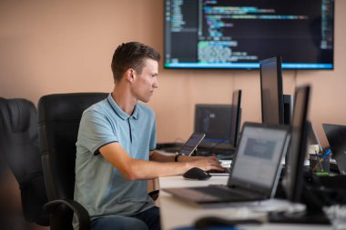 Genç bir programcı ofisinde masasında oturmuş, akıllı telefonlar için yenilikçi yeni uygulamaları test etmeye odaklanmış, yaratıcılık ve teknoloji ruhunu somutlaştırıyor..