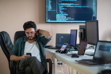 Bir programcı ofisinde otururken akıllı telefon uygulamalarını özenle test eder.