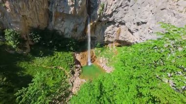 Bereketli yeşil ağaçlar ve ormanlarla çevrili kayalık bir uçurumdan şelalenin havadan çekilmiş videosu güneşli bir yaz gününde FPV insansız hava aracıyla ağır çekimde çekildi..