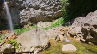 Bereketli yeşil ağaçlar ve ormanlarla çevrili kayalık bir uçurumdan şelalenin havadan çekilmiş videosu güneşli bir yaz gününde FPV insansız hava aracıyla ağır çekimde çekildi..