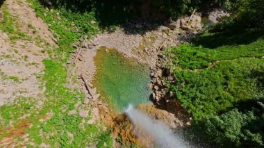 Bereketli yeşil ağaçlar ve ormanlarla çevrili kayalık bir uçurumdan şelalenin havadan çekilmiş videosu güneşli bir yaz gününde FPV insansız hava aracıyla ağır çekimde çekildi..
