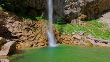 Bereketli yeşil ağaçlar ve ormanlarla çevrili kayalık bir uçurumdan şelalenin havadan çekilmiş videosu güneşli bir yaz gününde FPV insansız hava aracıyla ağır çekimde çekildi..