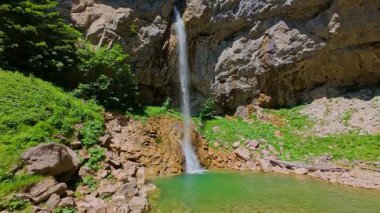 Bereketli yeşil ağaçlar ve ormanlarla çevrili kayalık bir uçurumdan şelalenin havadan çekilmiş videosu güneşli bir yaz gününde FPV insansız hava aracıyla ağır çekimde çekildi..